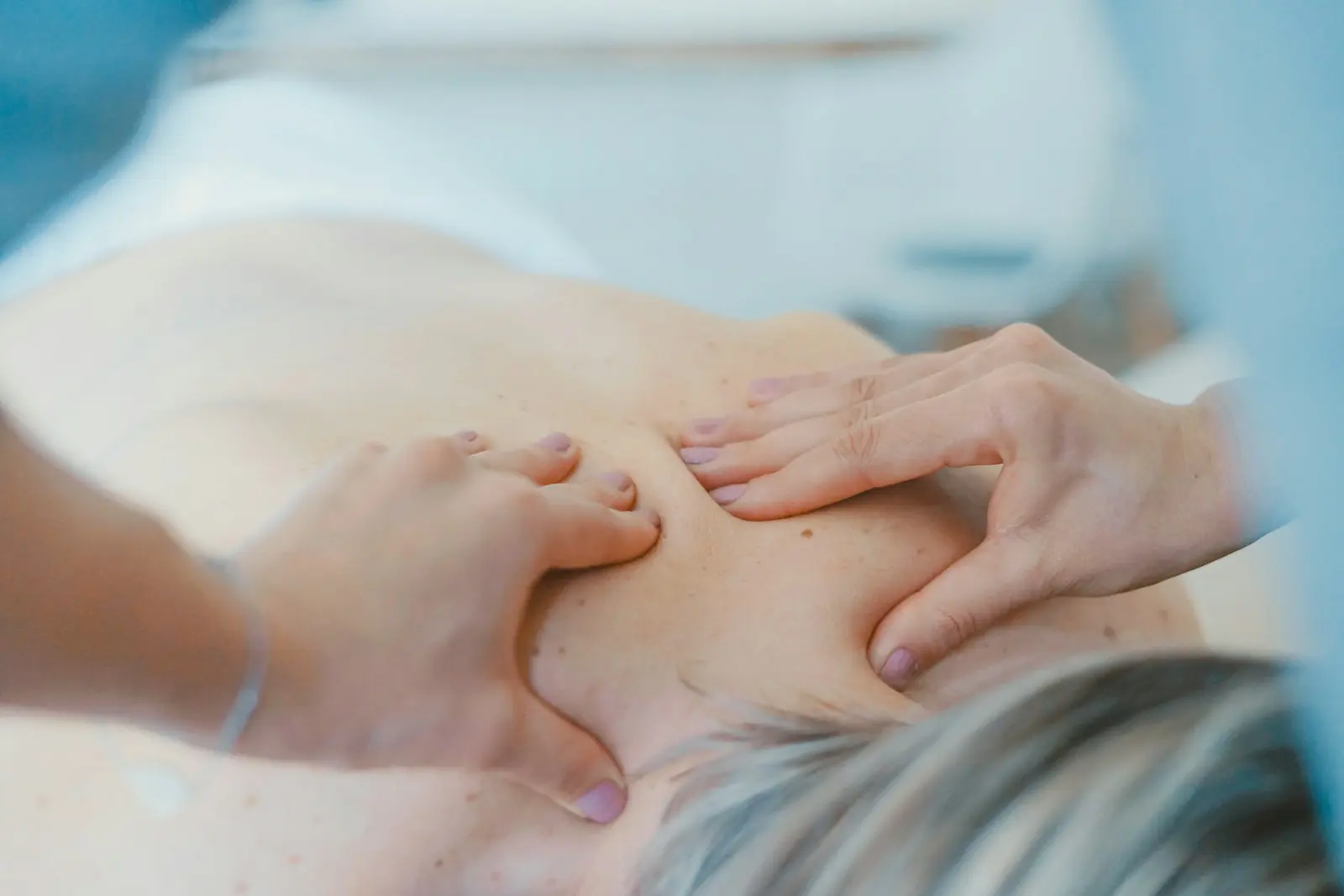 ベッドに横たわる女性の背中・肩をやさしくほぐすセラピストの手元。リラックスした施術のひとこま